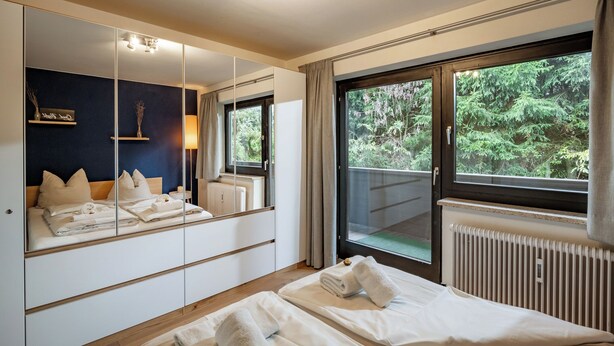 Une chambre d’hôtel avec un grand miroir, un lit où les serviettes sont soigneusement pliées, une fenêtre donnant sur un paysage verdoyant et un radiateur.