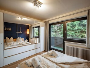 Een hotelkamer met een grote spiegel, een bed met keurig opgevouwen handdoeken, een raam met uitzicht op groen en een radiator.