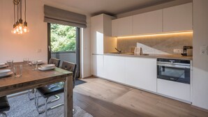 Une cuisine moderne avec des meubles blancs, un four encastré et un coin repas comprenant une table et des chaises en bois.