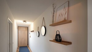 Un couloir avec une porte en bois, une moquette bleue et des étagères murales ornées d’objets décoratifs.