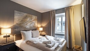 A hotel room with a large bed, two bedside lamps, a painting on the wall, a window with curtains, and a small rug. - Modern flat in the centre of Hopfgarten with 2 bedrooms (Hopfgarten)