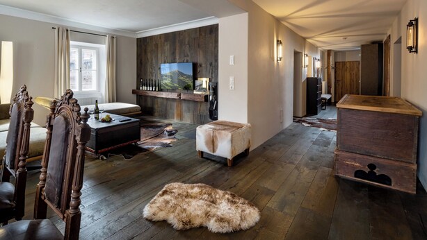 A spacious living room with a wooden floor, a large flat-screen TV mounted on a wooden wall, a cozy seating area with a sofa and chairs, and a rustic wooden cabinet. - Modern flat in the centre of Hopfgarten with 2 bedrooms (Hopfgarten)