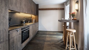 A modern kitchen with wooden cabinets, a built-in oven, and a bar area with stools. - Modern flat in the centre of Hopfgarten with 2 bedrooms (Hopfgarten)