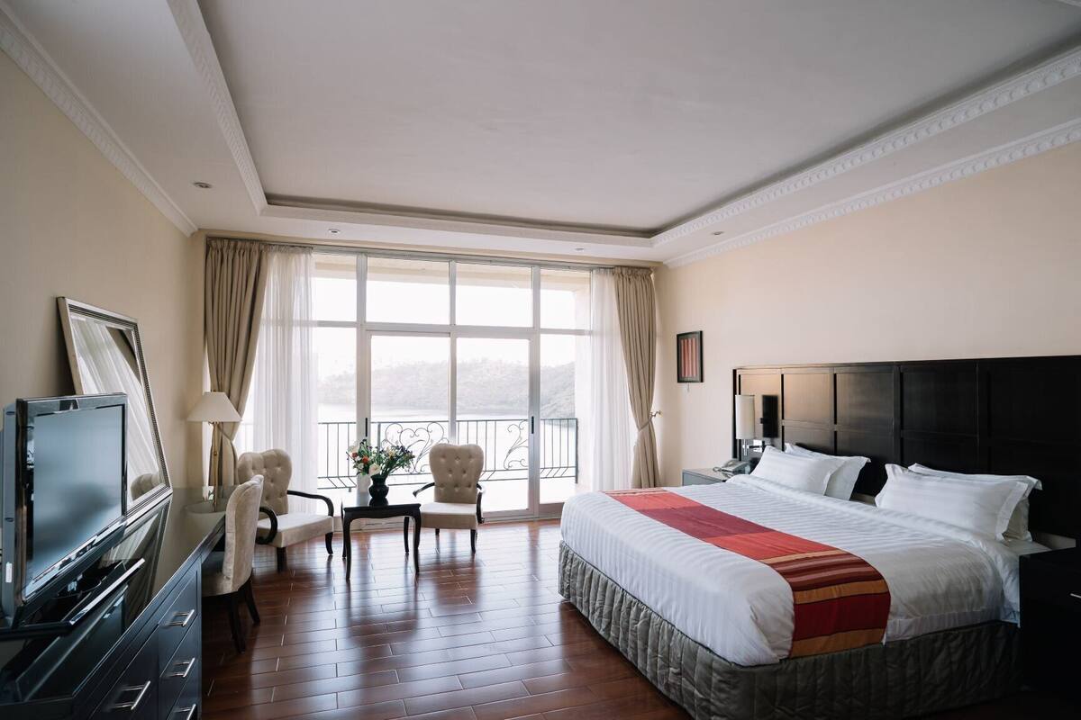 Habitación de hotel con una cama grande, televisión, escritorio con silla y balcón con vistas.