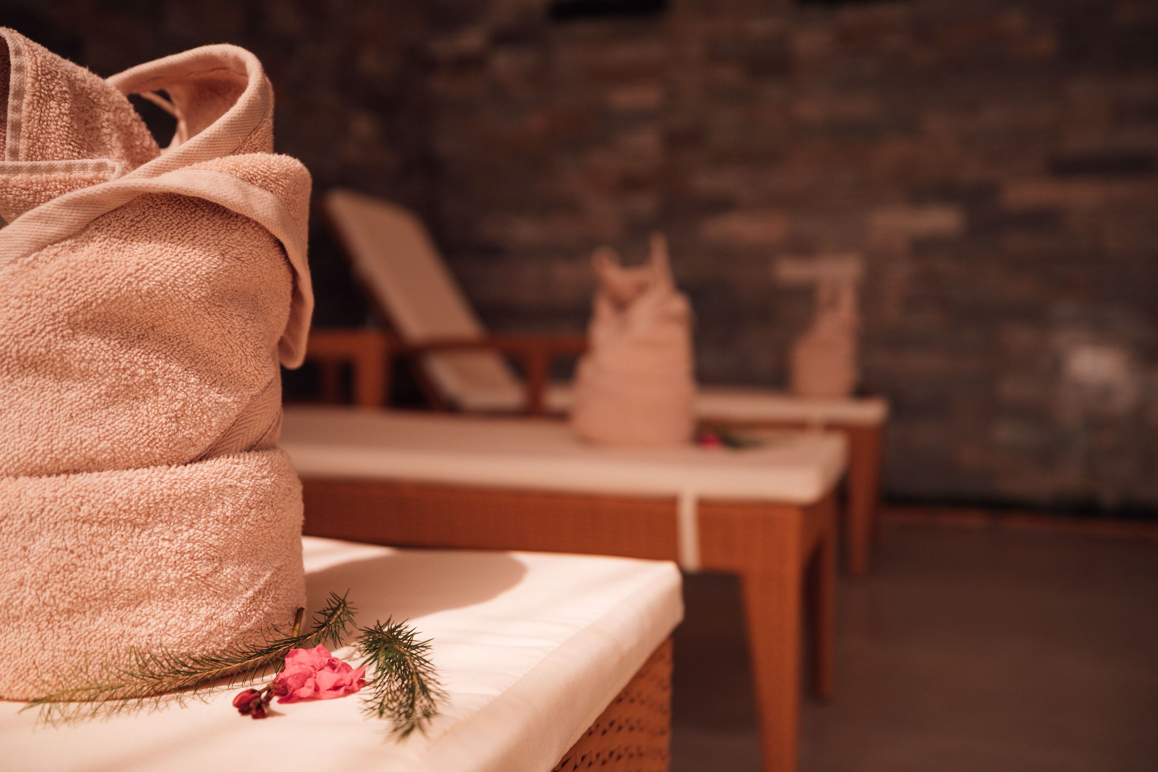 A spa room with a towel, a bottle, and a decorative pine branch on a wooden bench.