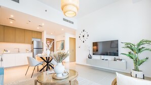 Een moderne woonkamer met een ronde glazen tafel, een bank en een aan de muur bevestigde televisie.