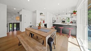 A modern kitchen with a wooden dining table, red bar stools, and pendant lighting. - Creekside Haven Family-Friendly Squamish Home (Squamish)