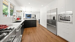 A modern kitchen with white cabinetry, stainless steel appliances, and wooden flooring. - Creekside Haven Family-Friendly Squamish Home (Squamish)
