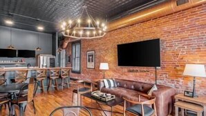 Un espace de vie moderne avec un mur en briques, un canapé en cuir, des meubles en bois et un téléviseur à écran plat.