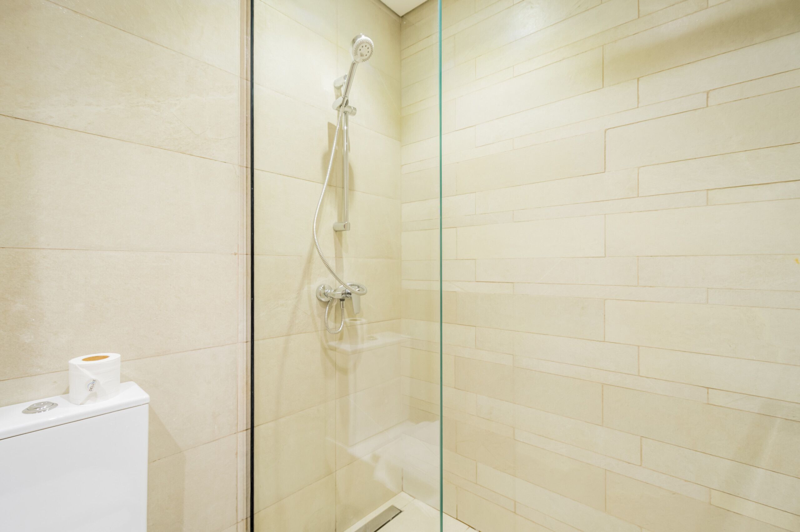Een douche met glazen wand, een handdouche en een kraan op de muur.