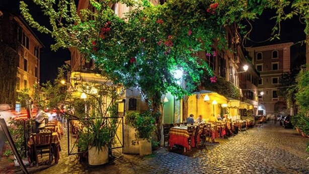 A cobblestone street lined with outdoor seating at a restaurant, surrounded by buildings with warm lighting. - Authentic Architectural Gem in the Heart of Rome
 (Roma)