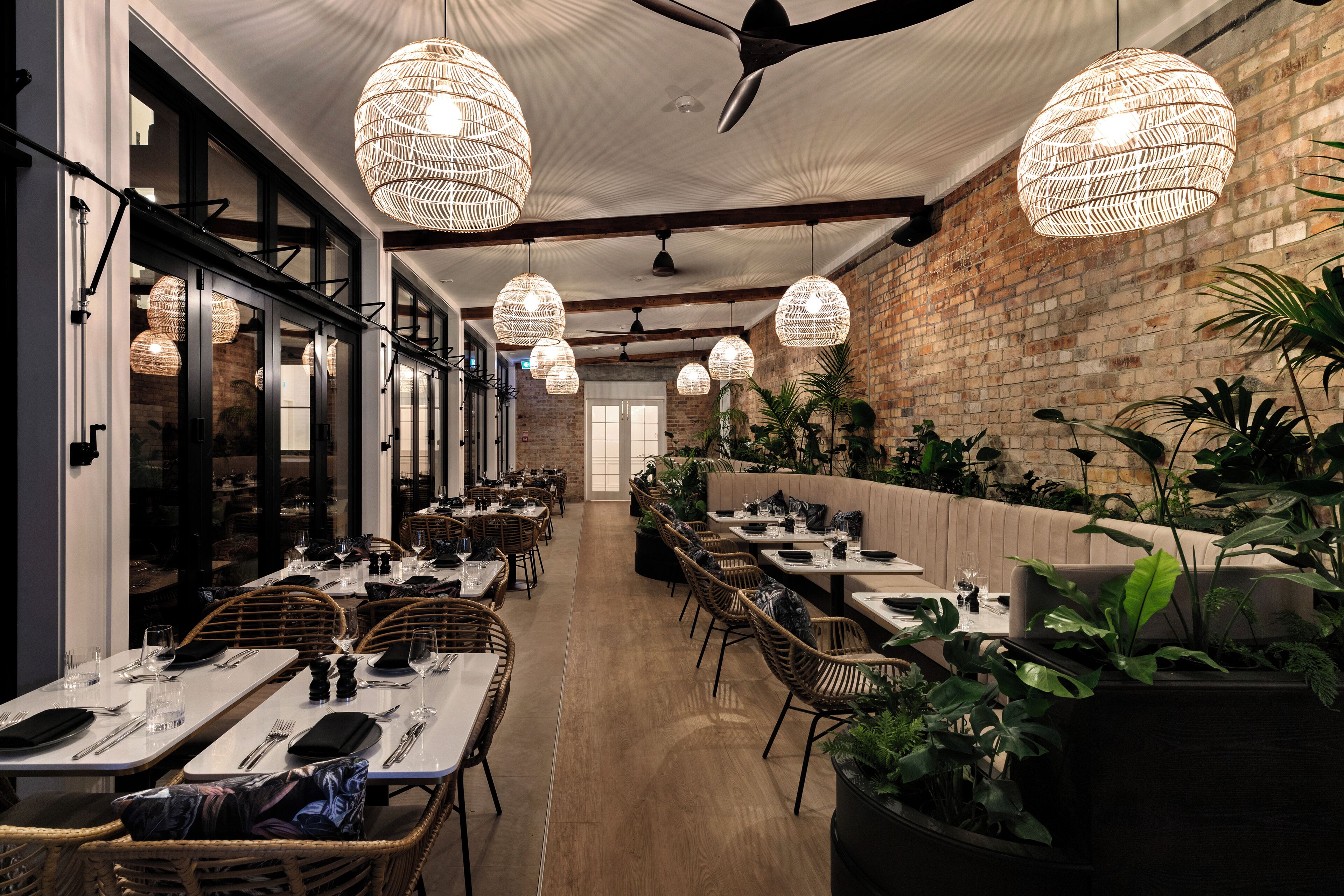 Un restaurante con mesas largas, sillas de mimbre y lámparas colgantes de mimbre.