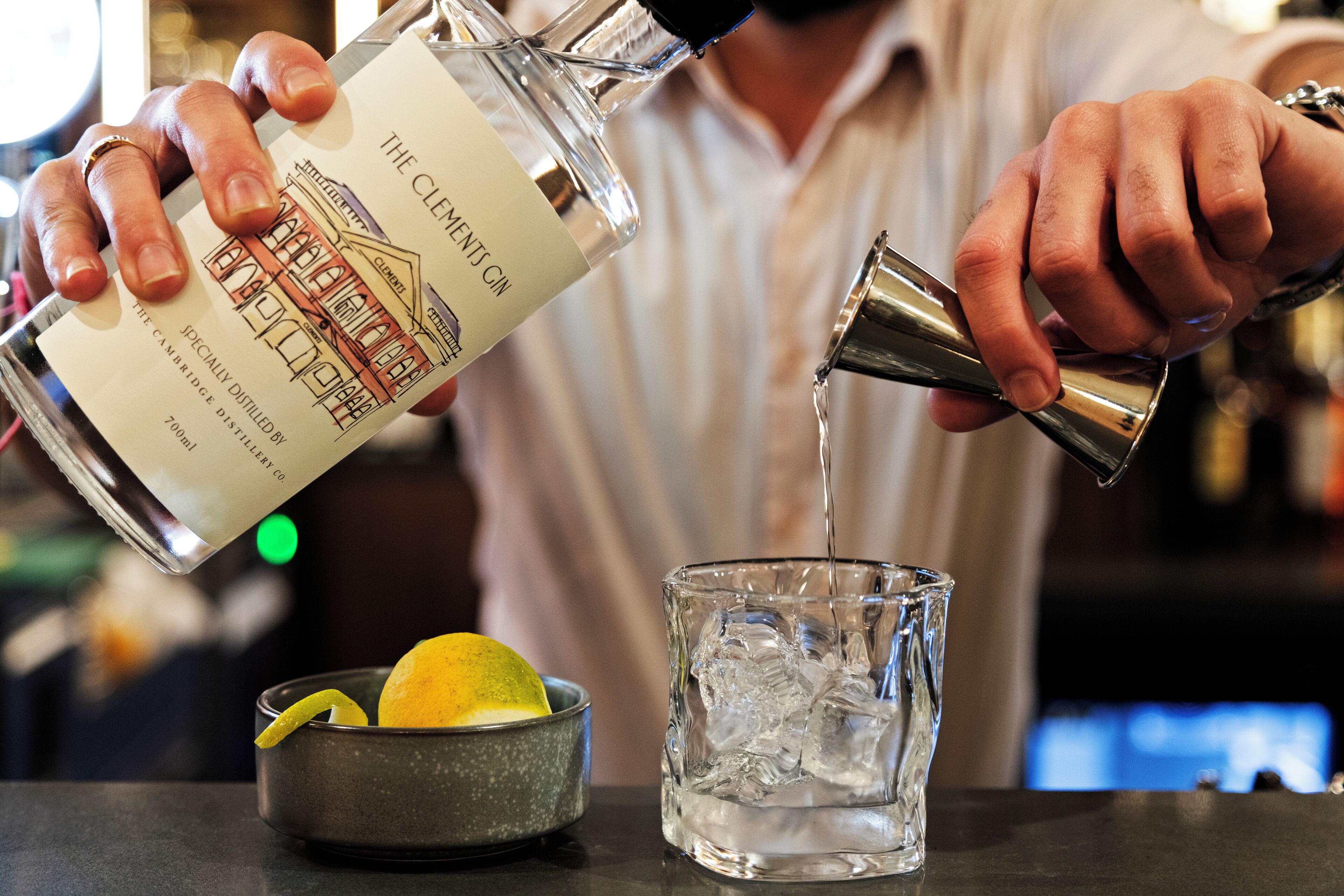 A person pouring a clear liquid from a bottle into a glass with ice cubes.