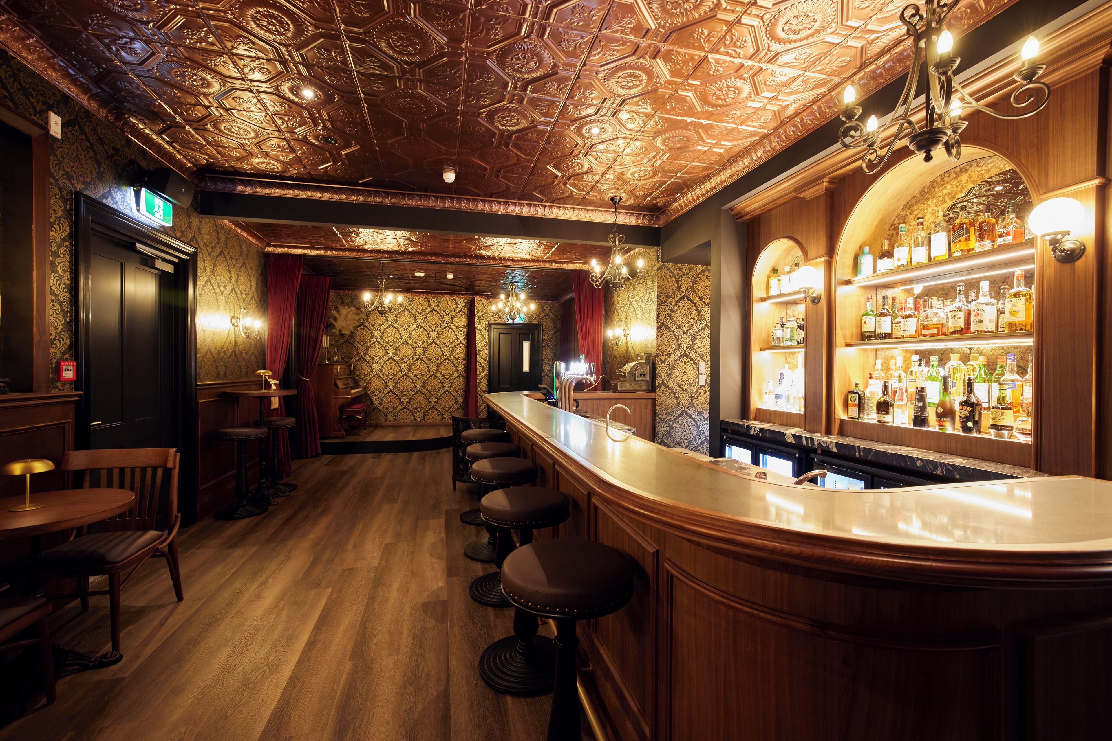 A bar area with a wooden bar counter, stools, and a well-stocked liquor shelf.