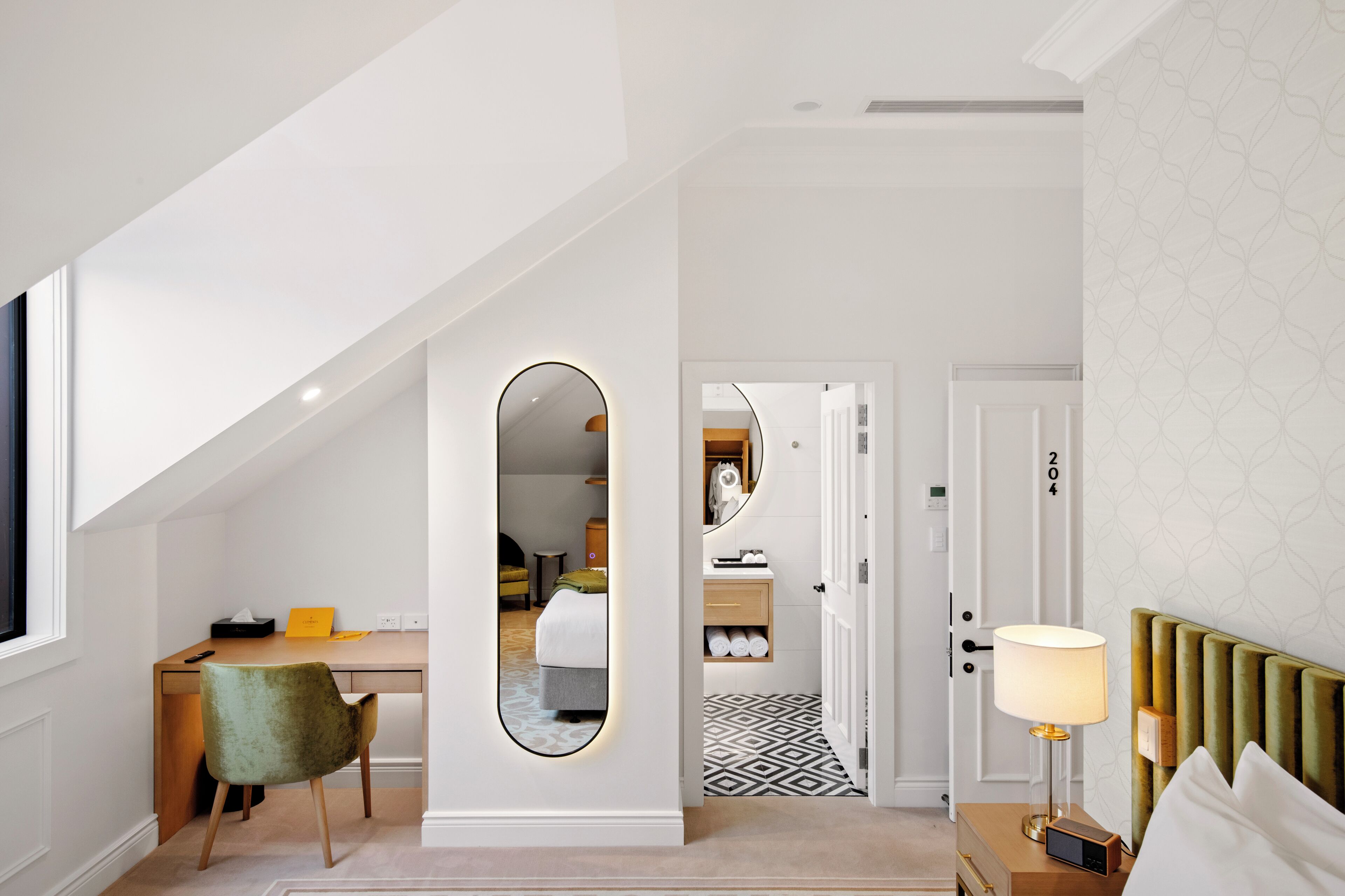 A modern hotel room with a desk, chair, and a large mirror.