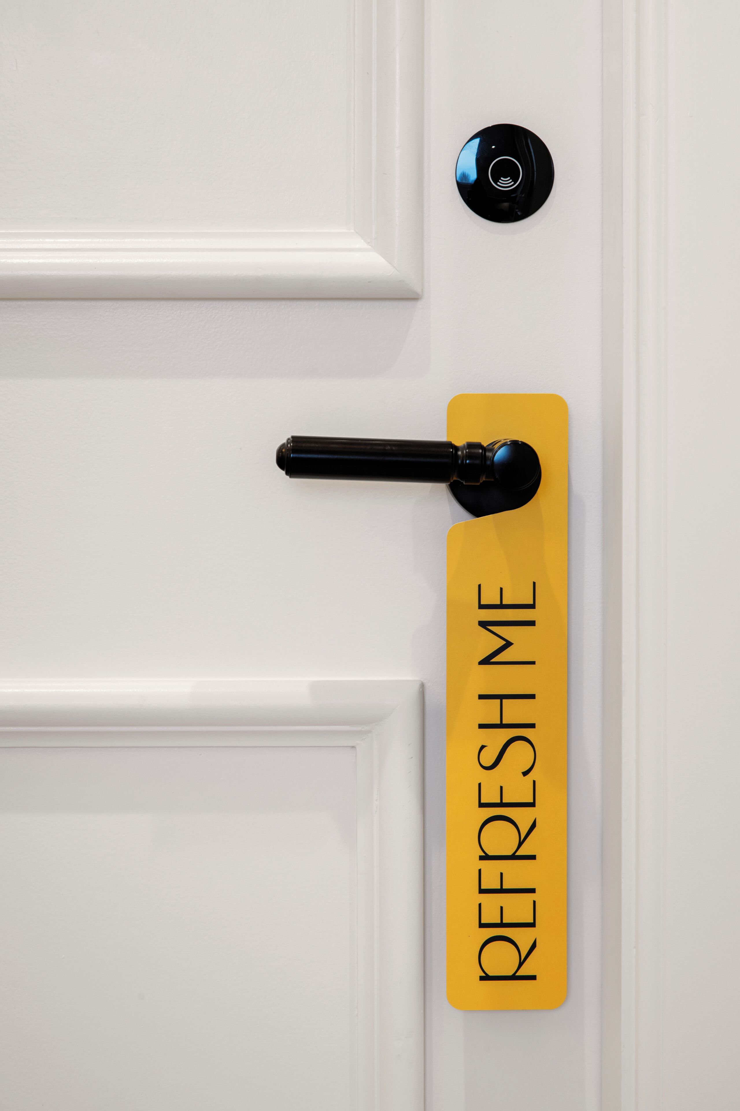 Una puerta blanca con picaporte negro y un letrero amarillo que dice "REFRESH ME".