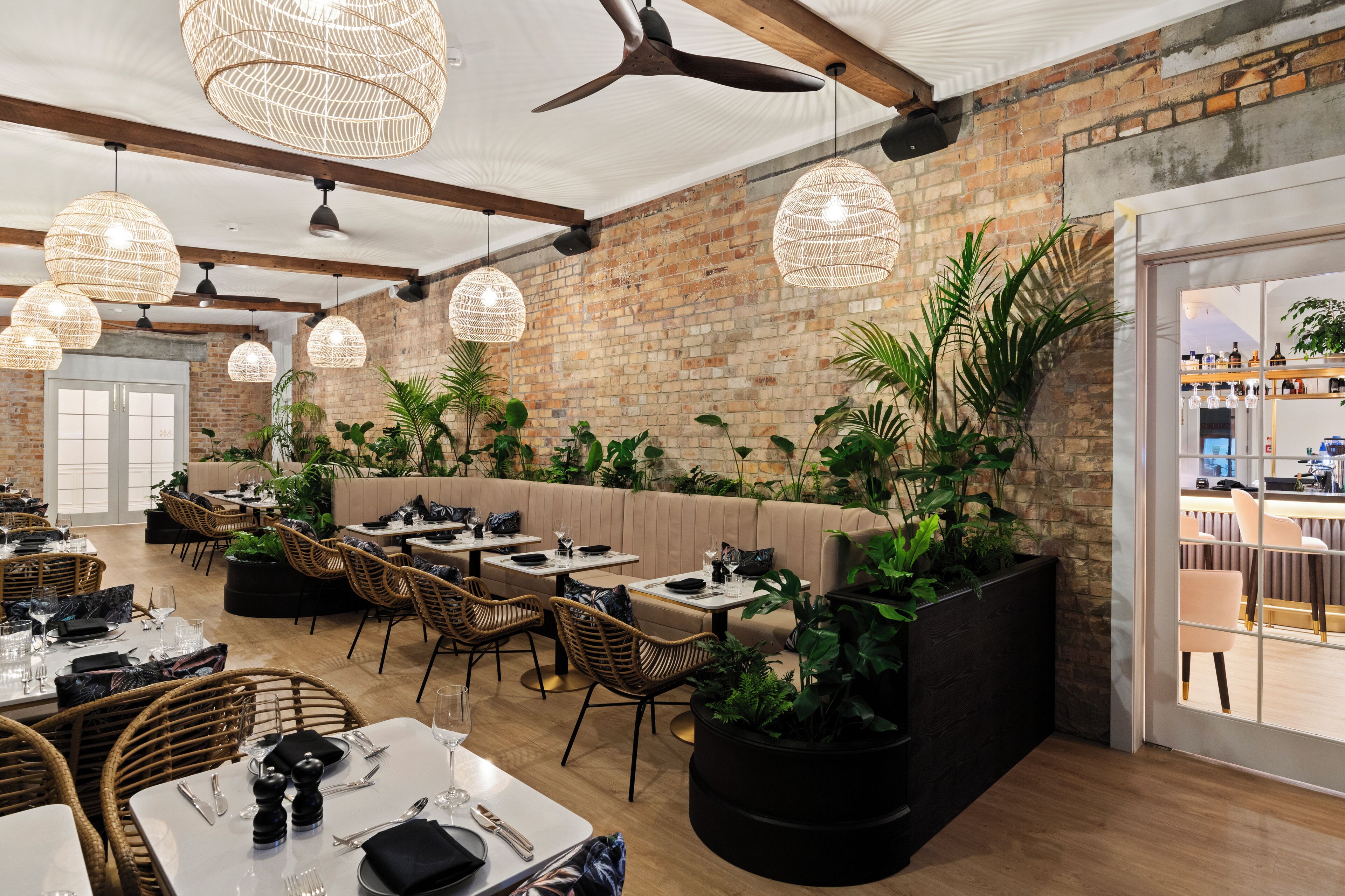 A restaurant with brick walls, wicker furniture, and hanging wicker lamps.
