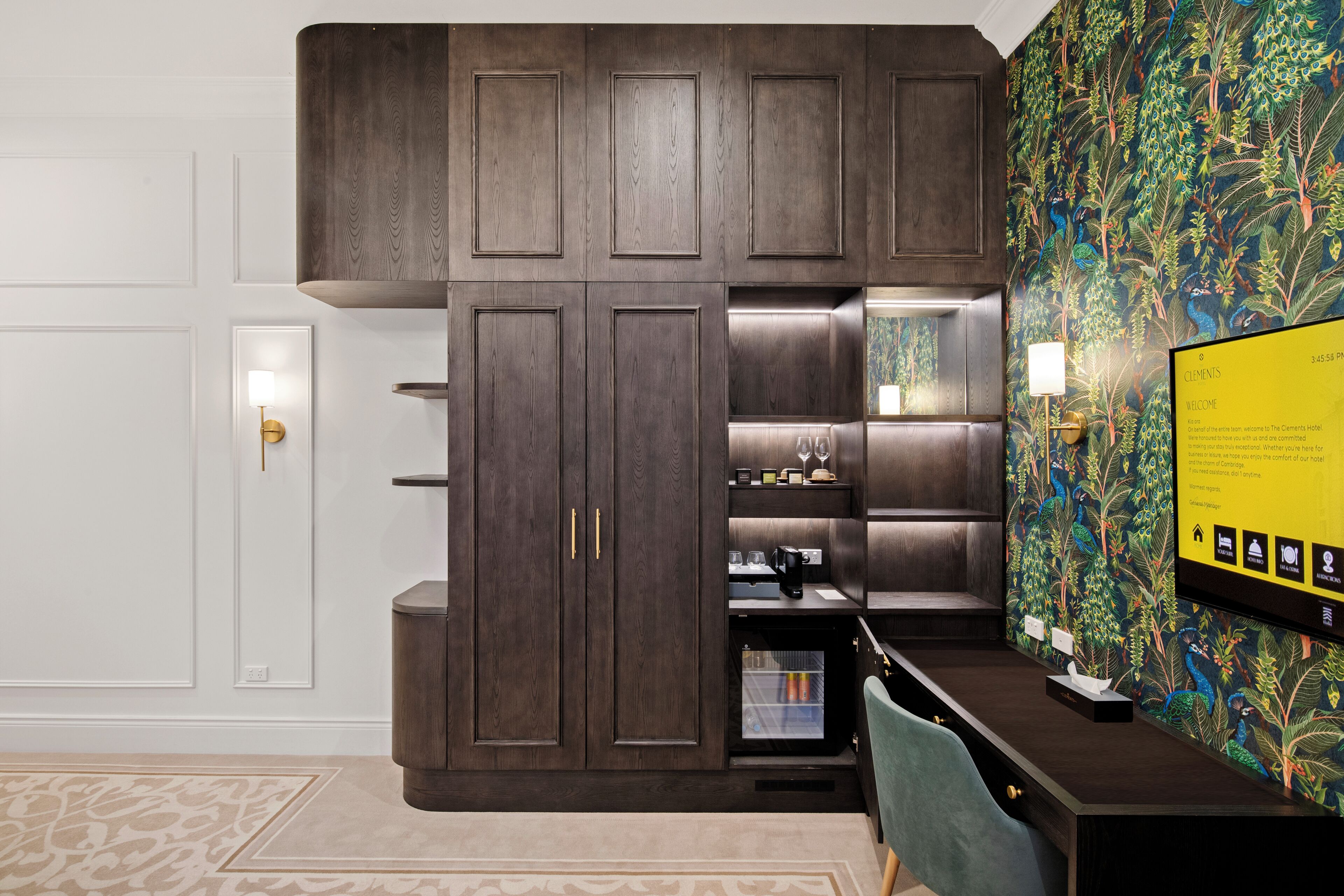 A modern hotel room with a dark wood cabinet, a flat-screen TV, and a vibrant floral wallpaper.