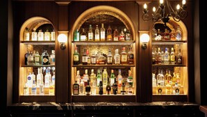 Un espace bar avec des étagères remplies de bouteilles d’alcool, un comptoir en marbre et un lustre.