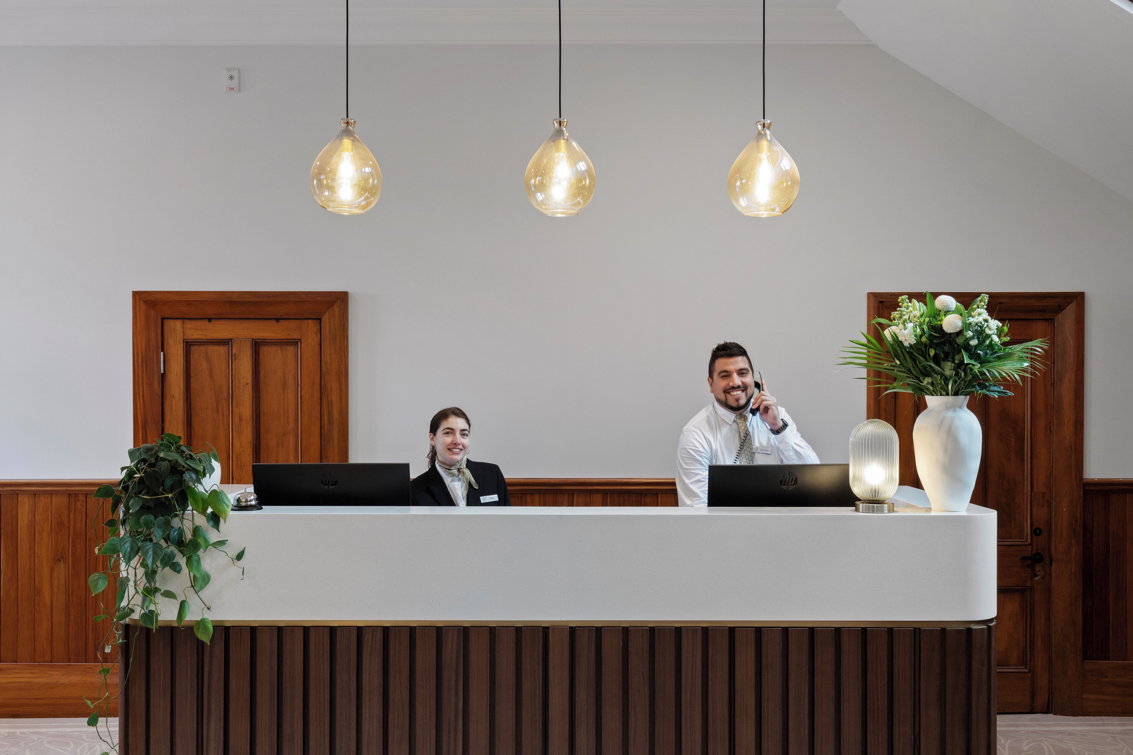 A reception desk with two staff members, a wooden door, and a plant.