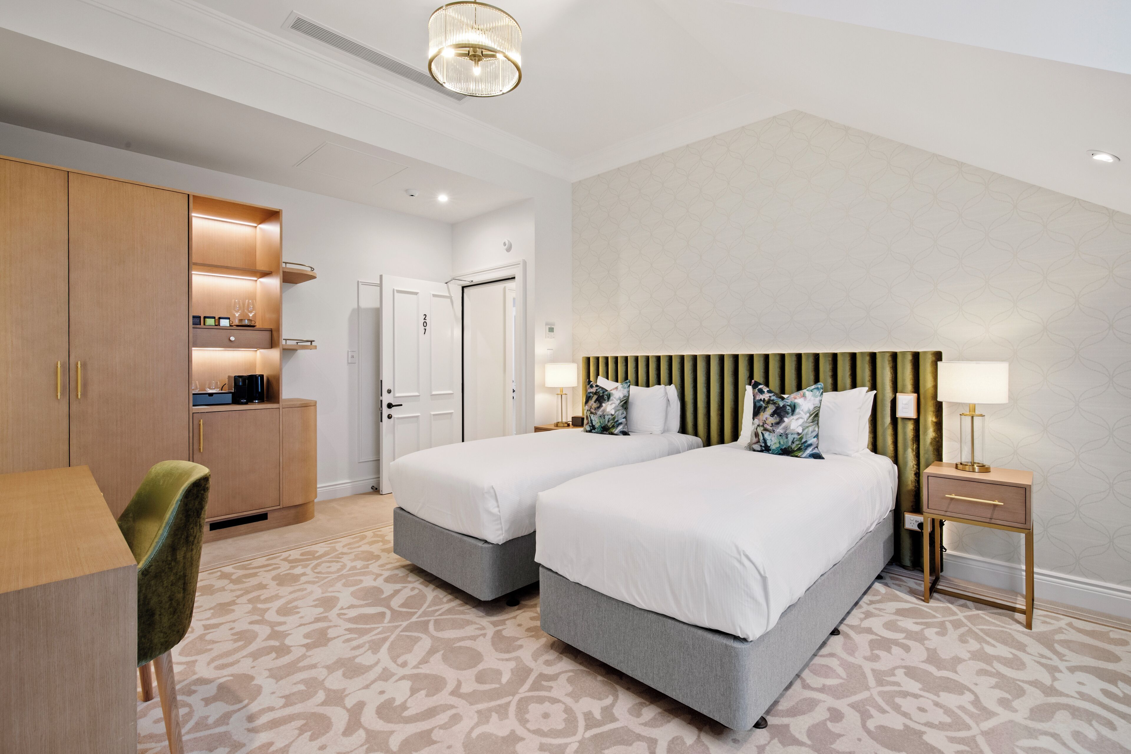 A hotel room with two beds, a desk, a chair, a nightstand, and a patterned carpet.