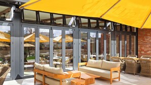 Un espace extérieur aménagé avec des sièges, un parasol jaune, des meubles en osier et une porte vitrée donnant sur un patio.