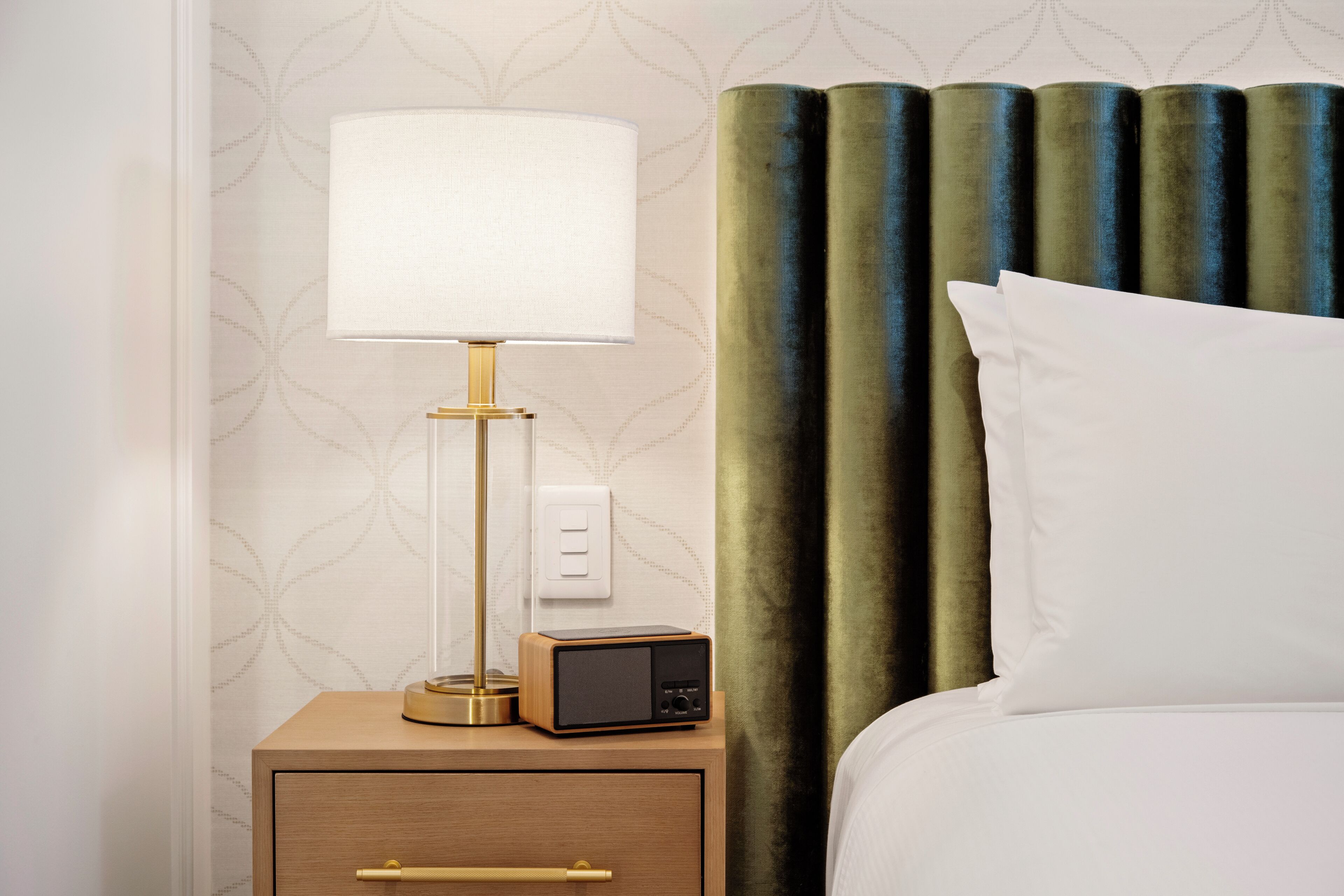 A neatly made bed with a white pillow and a green curtain backdrop.