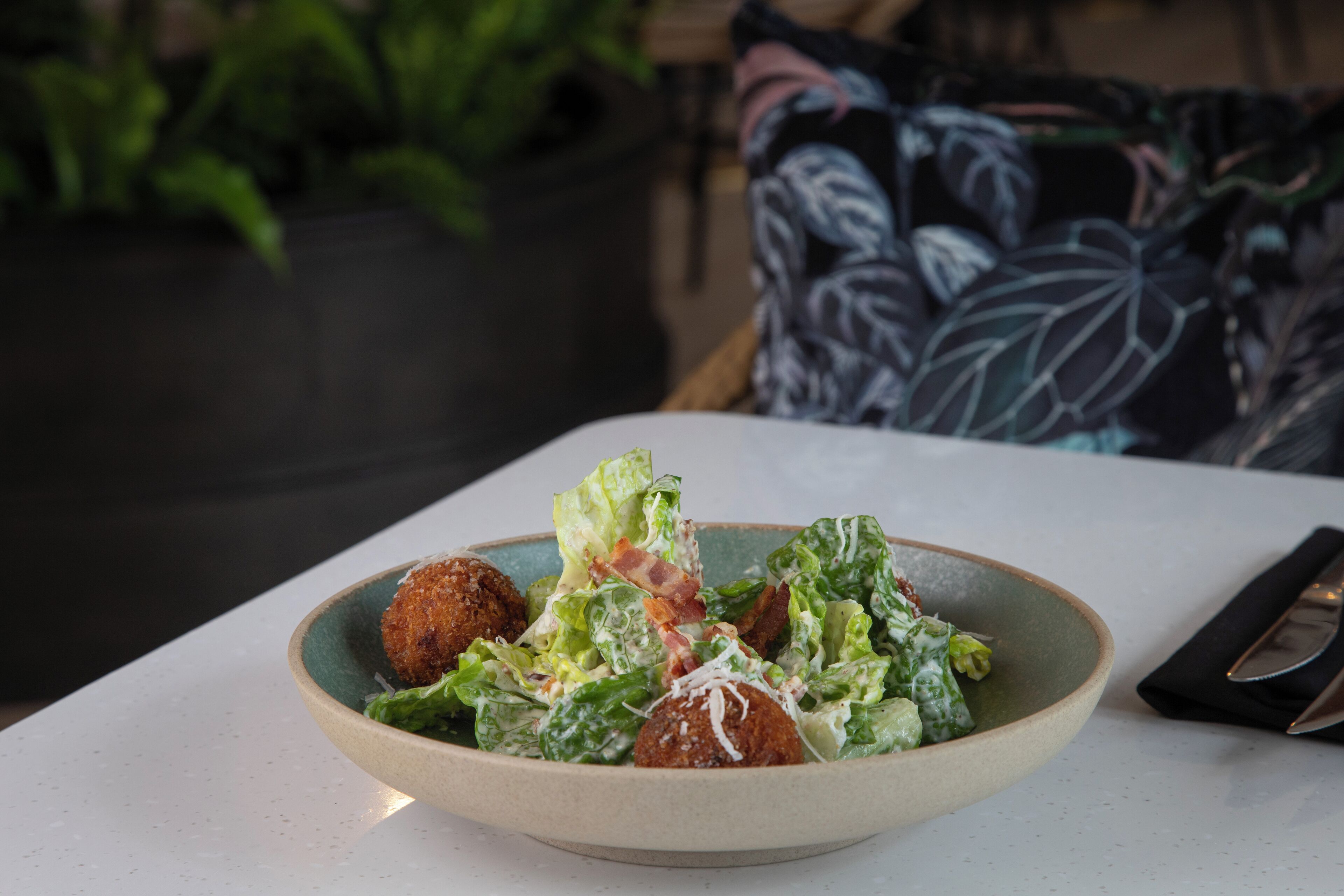 A bowl of salad with lettuce and croutons on a table.