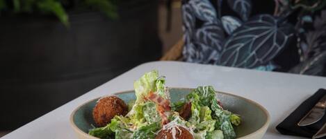 A bowl of salad with lettuce and croutons on a table.