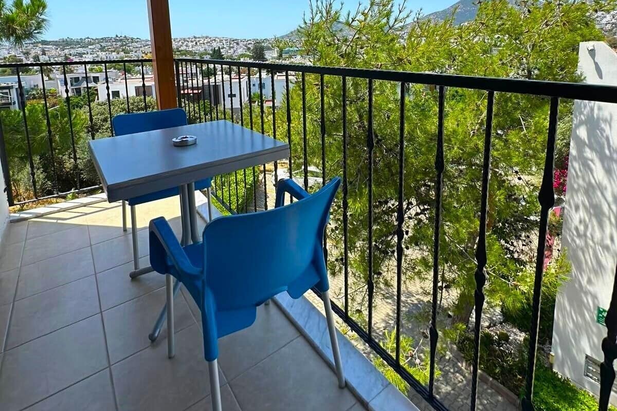 A balcony with a table and chairs, a tiled floor, and a view of a cityscape and hills.