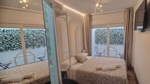 A bedroom with two beds, a TV, and a balcony with chairs and a table. - La Maison del Mar: 1º4 Deluxe Room with Terrace/Bathroom near the Beach (Málaga)