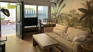 A living room with a sofa, coffee table, TV, and a mural of a tropical scene. - La Maison del Mar: 1º4 Deluxe Room with Terrace/Bathroom near the Beach (Málaga)
