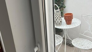 A sliding glass door leading to a small outdoor patio area with a white metal table and chairs, a potted plant, and a stack of terracotta pots. - La Maison del Mar: 1º4 Deluxe Room with Terrace/Bathroom near the Beach (Málaga)