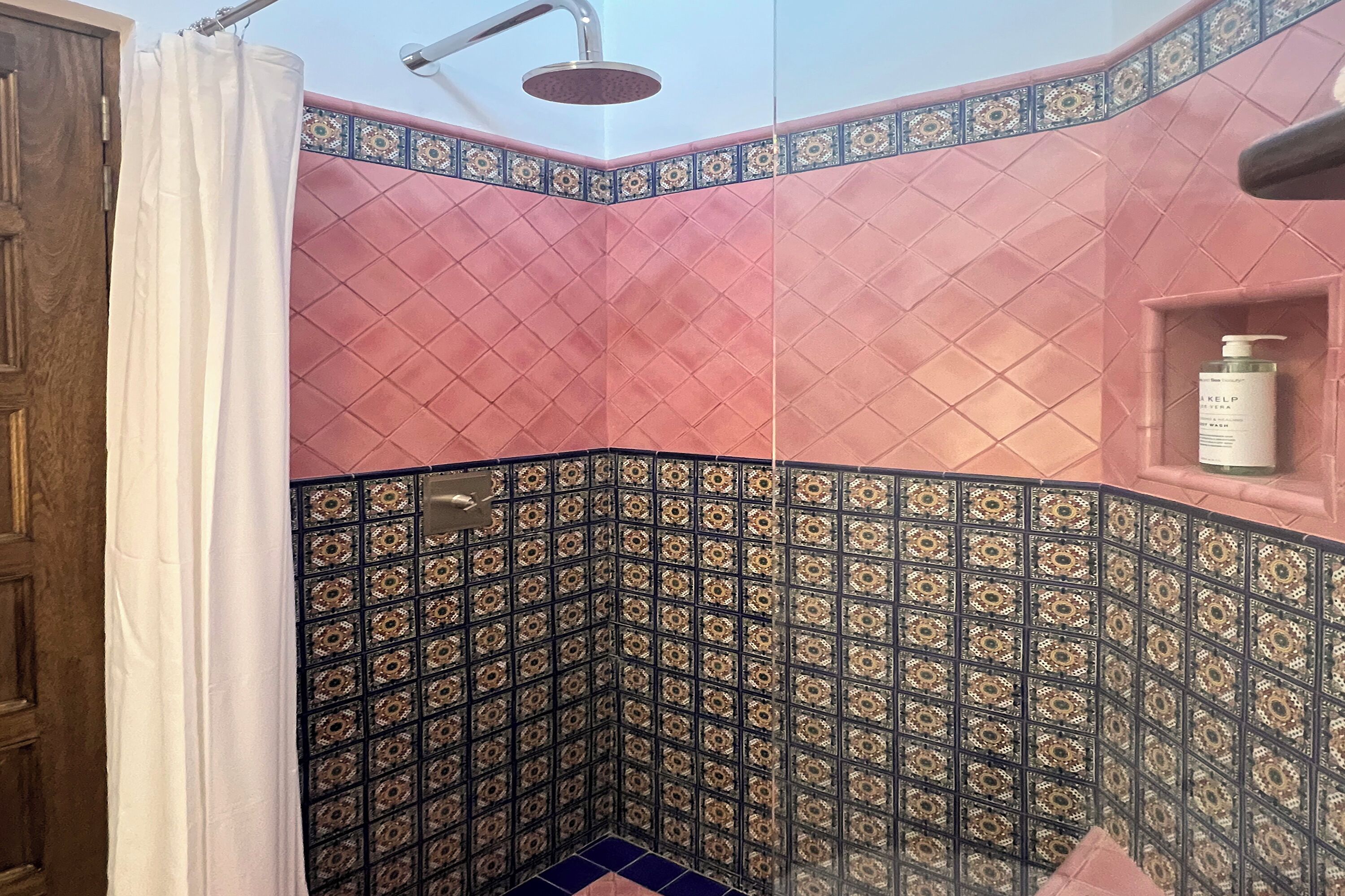 Een badkamer met roze en blauwe betegelde muren, een douche en een plank met een fles.