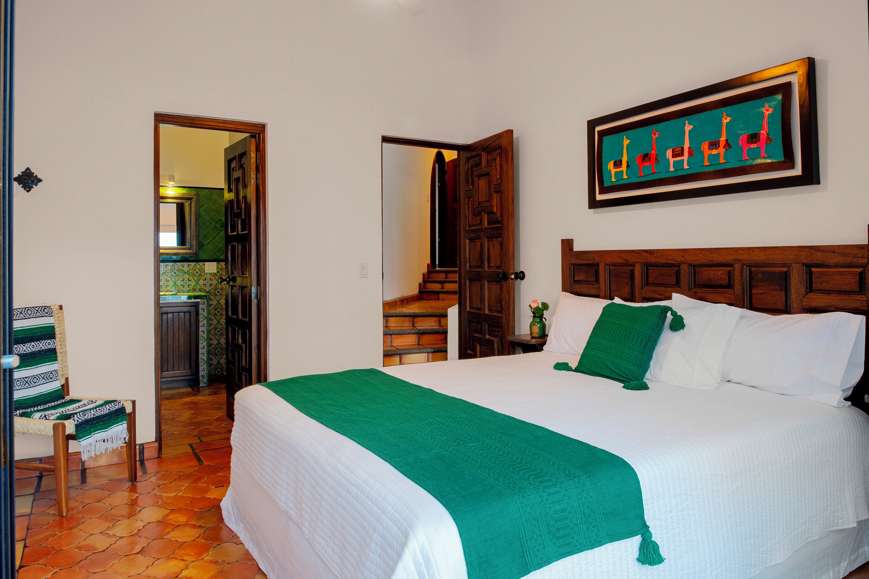 Habitación de hotel con una cama grande, una manta verde, un cabecero de madera y un cuadro de un animal colgado en la pared.