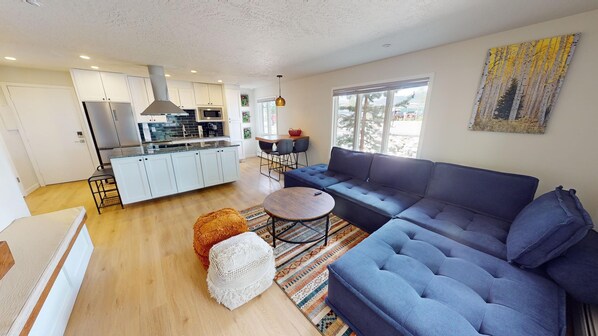 A modern living room with a blue sofa, a round coffee table, and a kitchen area with white cabinets and a stove. - Updated End Unit In Town! Walk to Coffee, Amp, Marina, Parks, Rec Path, Eats (Dillon)