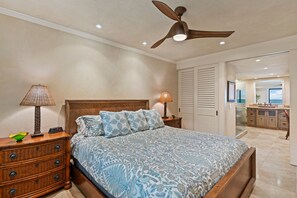 A bedroom with a bed, a nightstand, a dresser, a ceiling fan, and a view of the bathroom. - Makena Surf, #e-203 2 Bedroom Condo by RedAwning (Kihei)