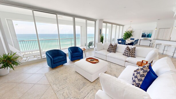 A spacious living room with a white sofa, two blue armchairs, and a coffee table. A large window offers a view of the ocean. - Oceania 807 3 Bedroom Condo by RedAwning (Destin)