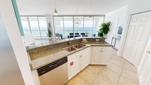 Enjoy ocean views from this kitchen's scenic balcony, featuring a granite countertop, stainless steel sink, and white cabinetry.