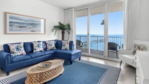 A living room with a blue sofa, a coffee table, and a view of the ocean through large sliding glass doors. - ☀️Beachfront|Gulf Views|Pools|3BR Summerwind 1203☀️ (Navarre Beach)