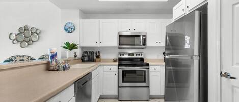 Une cuisine moderne avec des meubles blancs, des appareils électroménagers en acier inoxydable et un sol carrelé.