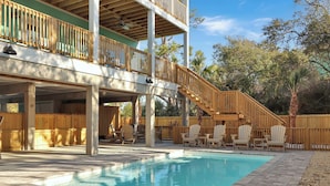 Un espace piscine avec des chaises longues en bois, une terrasse en bois dotée d’un escalier, et une vue sur les arbres.