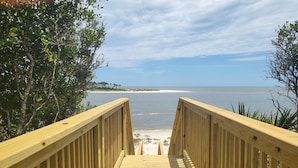 Une promenade en bois mène à une plage d’où l’on a une vue dégagée sur l’océan et le rivage lointain.