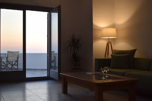 Une pièce dotée d’une porte-fenêtre coulissante donnant sur un balcon, d’un canapé vert, d’une table basse en bois avec des verres, et d’un lampadaire.