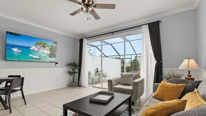 Ein modernes Wohnzimmer mit großem Fenster, Deckenventilator, Essbereich mit Tisch und Stühlen sowie einer Couch mit Kissen.