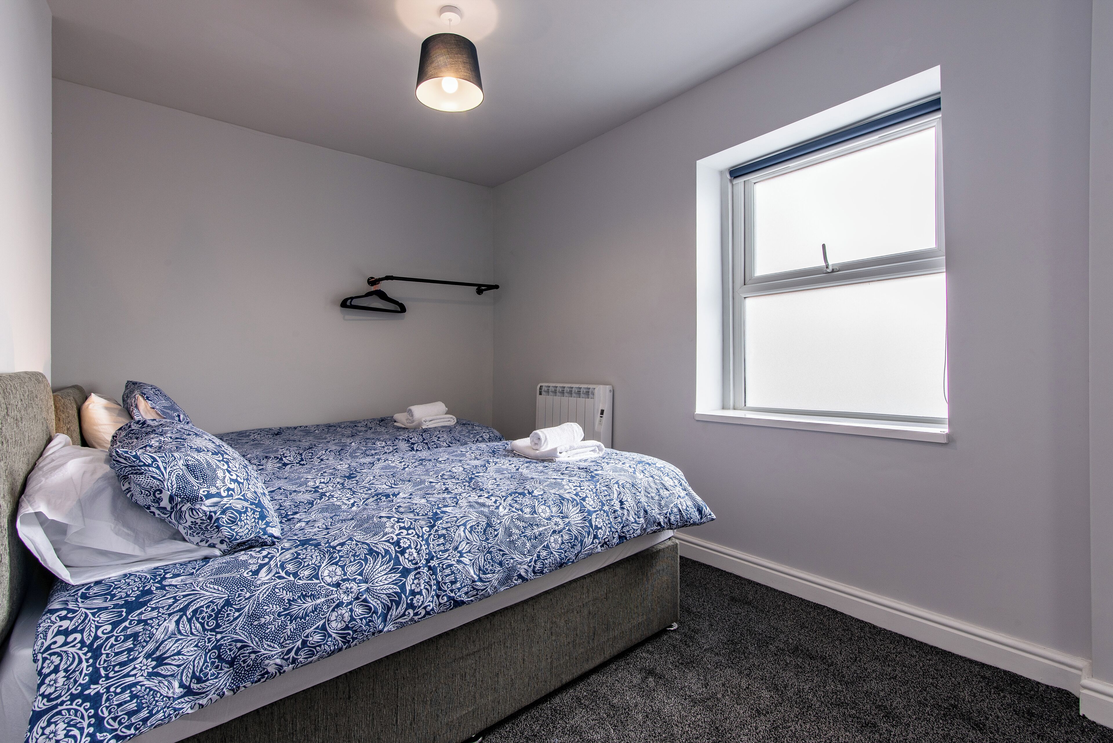 A bedroom with a bed, a radiator, a window, and a hanging light fixture.