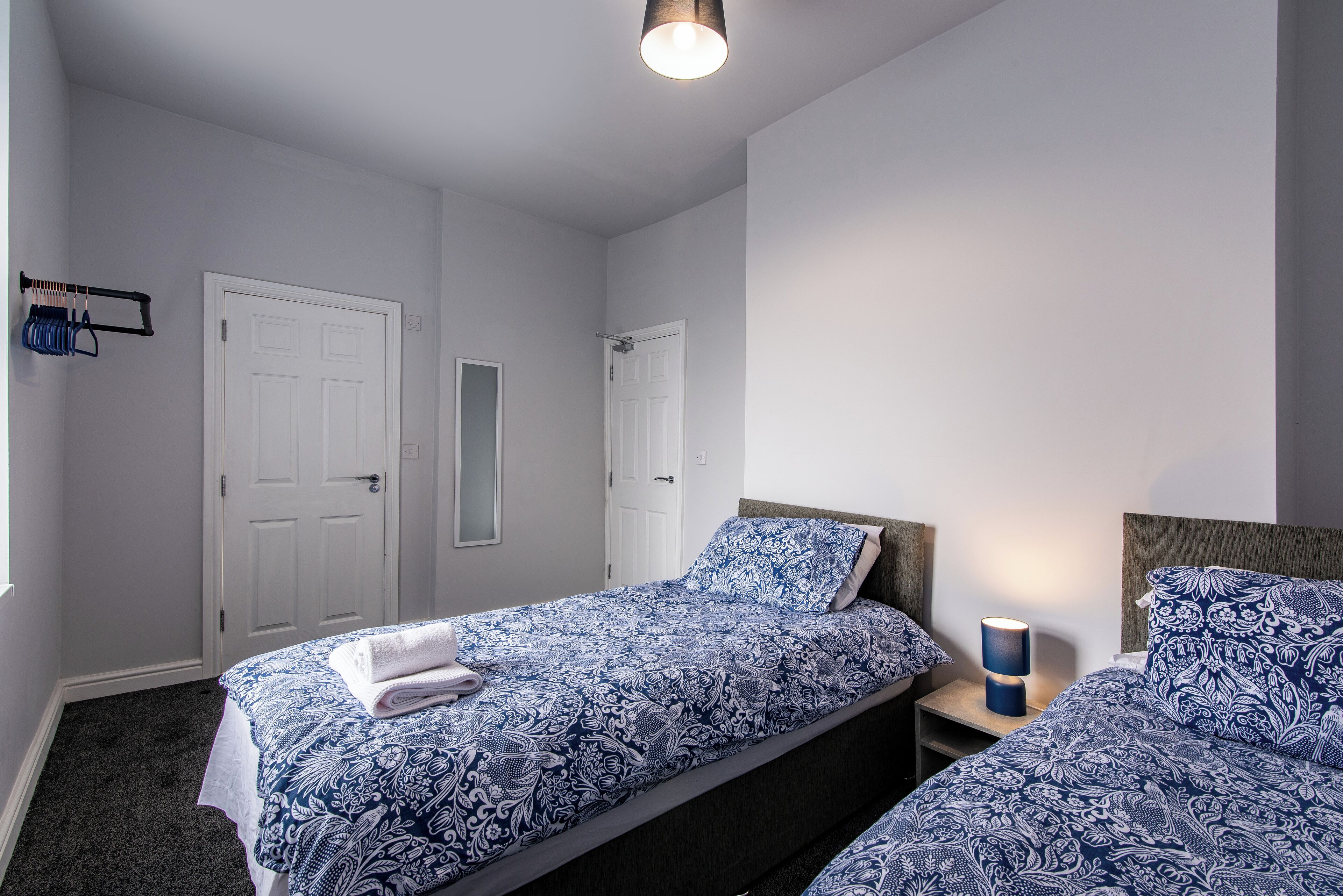 Un dormitorio con dos camas, paredes blancas e iluminación en el techo.