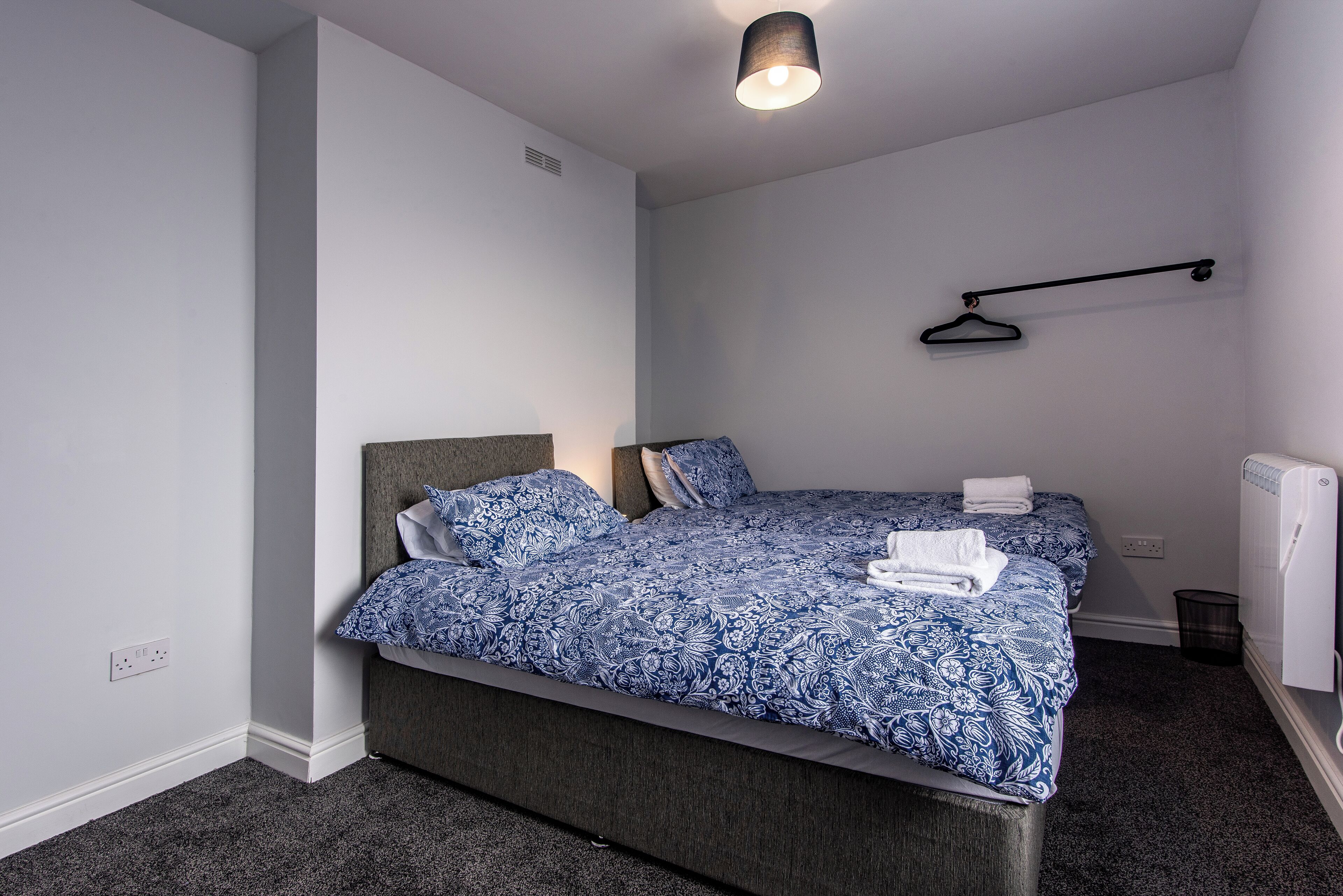 A bedroom with a bed, a hanging light fixture, a radiator, and a power outlet on the wall.