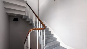 A staircase with white railings and a wooden handrail, leading to a landing with a black object on the wall.