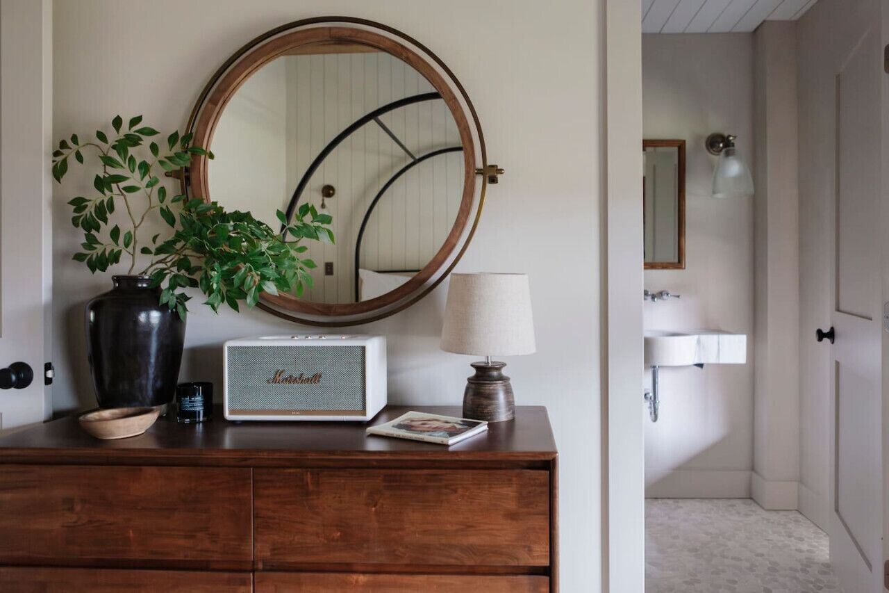 Een houten dressoir met spiegel, een radio, een lamp en een potplant.